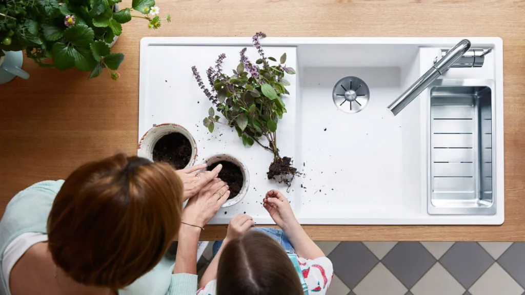 Frau und Kind pflanzen Lavendel an einer weißen Blanco Spüle