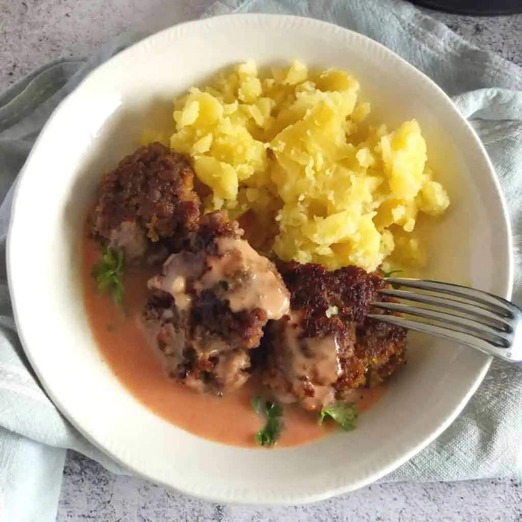 Frikadellen und Kartoffelpüree mit Rahmsauce auf einem Teller serviert