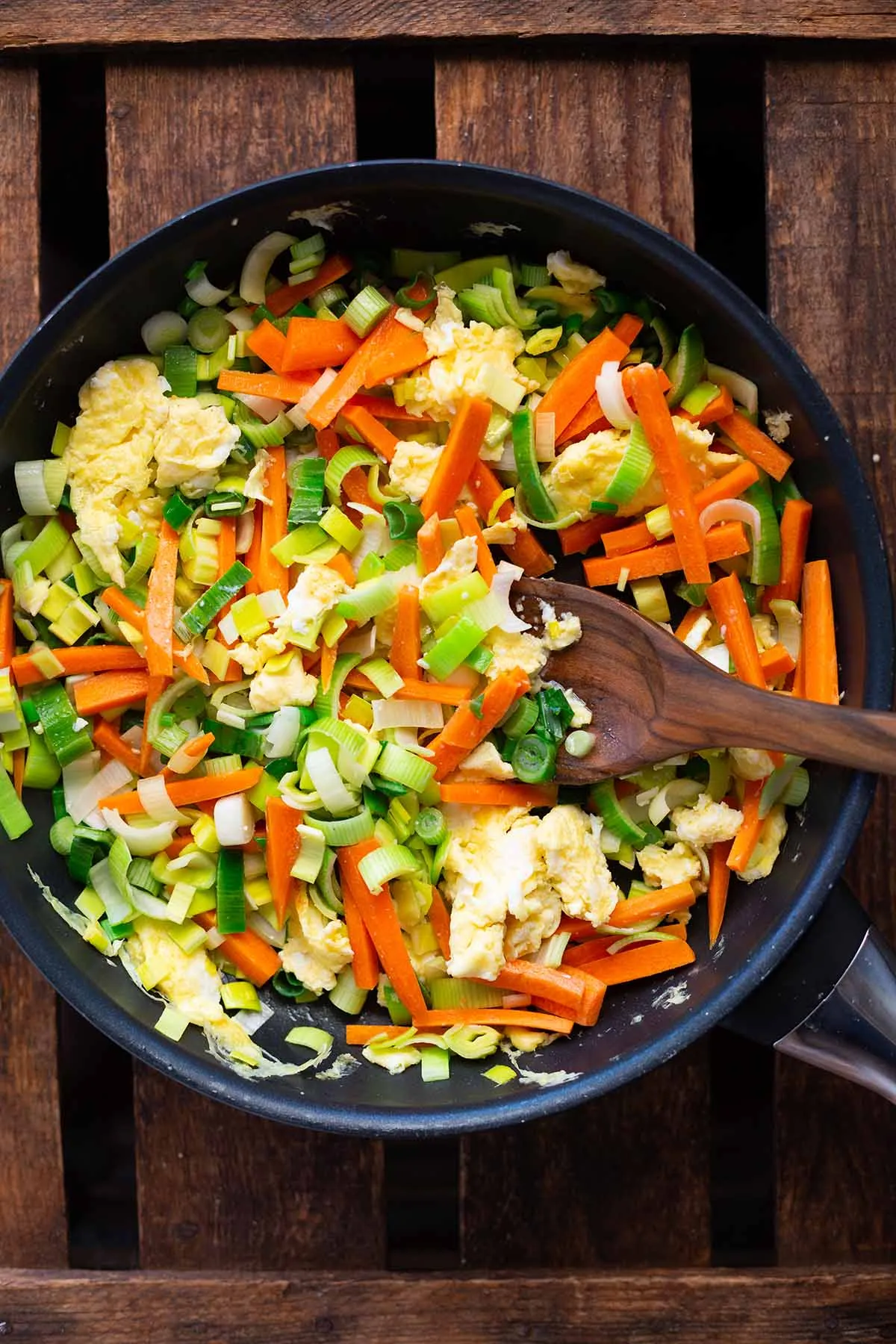 Frisch angebratenes Ei und verschiedene Gemüsesorten wie Karotten und Lauch in einer großen Pfanne, bereit für die Zubereitung der gebratenen Nudeln.