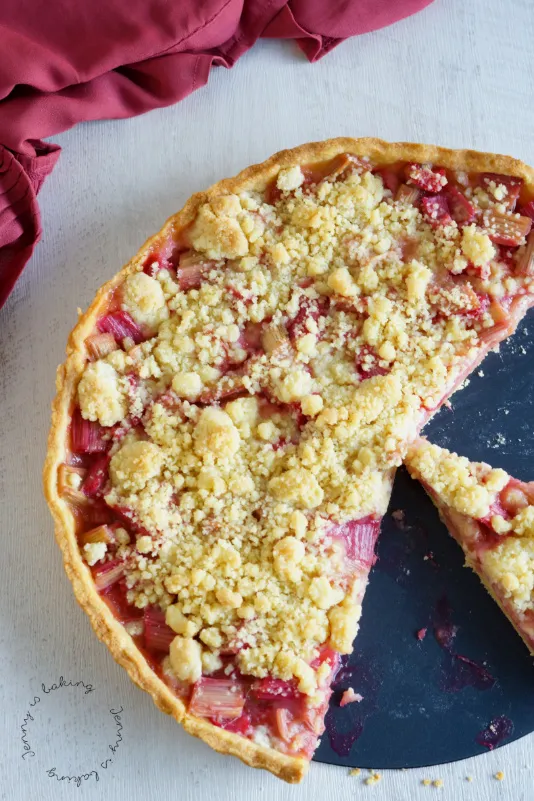 Frisch gebackene Rhabarber-Streuseltarte auf einem Holzbrett serviert, perfekt für die Kaffeetafel