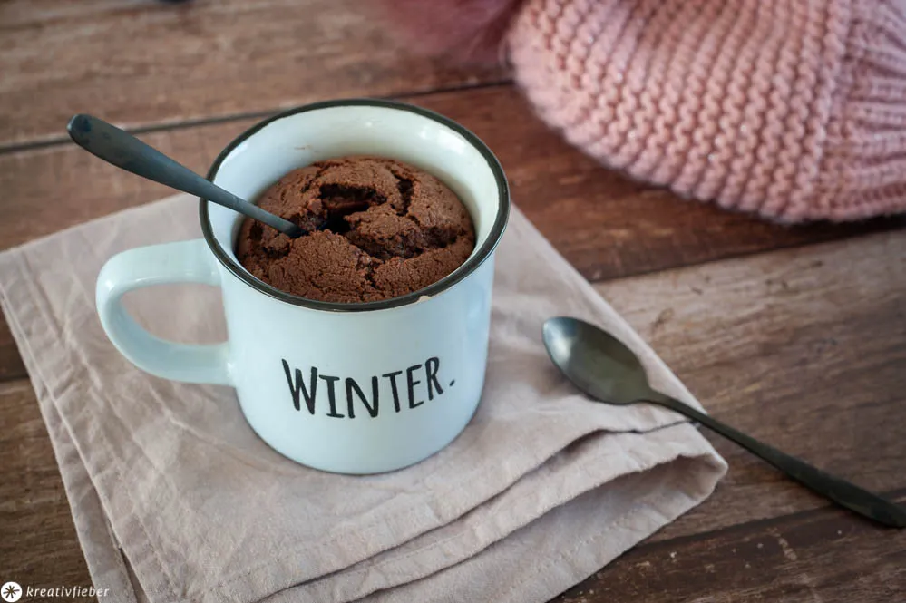 Frisch gebackener Schokoladen-Tassenkuchen aus dem Backofen, verziert mit Puderzucker auf einer hölzernen Unterlage, bereit zum Genießen.