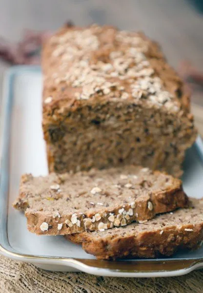 Frisch gebackenes Dinkel-Vollkornbrot in Scheiben geschnitten und mit Haferflocken bestreut, eine Scheibe mit Erdnussbutter und Bananen belegt.