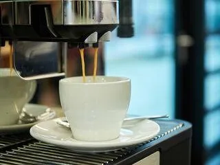 Frisch gebrühter Kaffee fließt aus einem modernen Kaffeevollautomaten mit Festwasseranschluss in eine Tasse im Büroambiente.