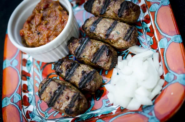 Frisch gegrillte Ćevapčići, appetitlich angerichtet mit gehackten Zwiebeln und Petersilie.