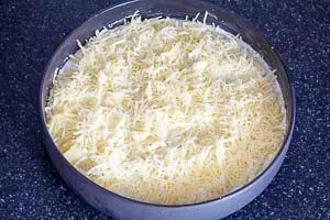 Frisch geriebener Emmentaler wird gleichmäßig über die Kartoffelschichten verteilt