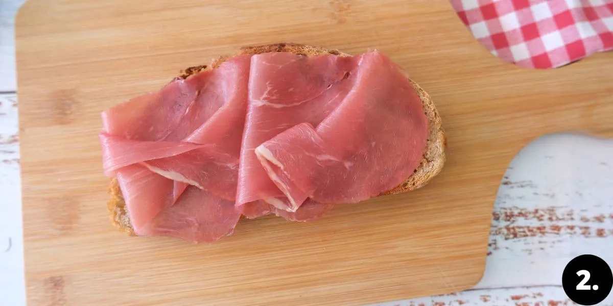 Frisch geröstetes Roggenbrot, belegt mit saftigen Scheiben geräuchertem Schinken, bereit für das Spiegelei. Ein wichtiger Schritt im Strammer Max Rezept.