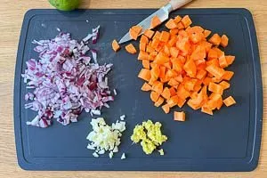 Frisch geschnittene Zwiebeln, Karottenwürfel, Knoblauch und geriebener Ingwer auf einem Schneidebrett, bereit für die Zubereitung der Suppe.