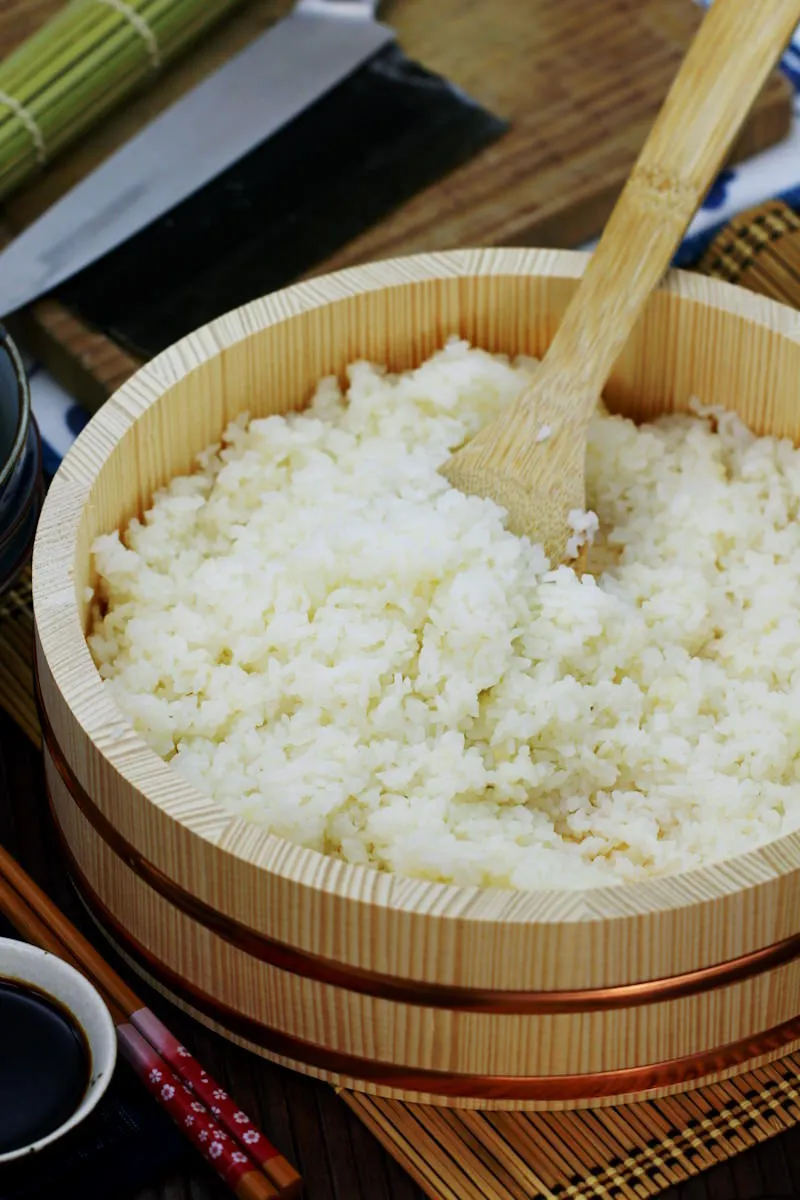 Frisch gewürzter Sushi Reis in einer Hangiri-Schale, mit einem Shamoji-Löffel vorsichtig vermengt, um die perfekte Konsistenz zu erzielen.