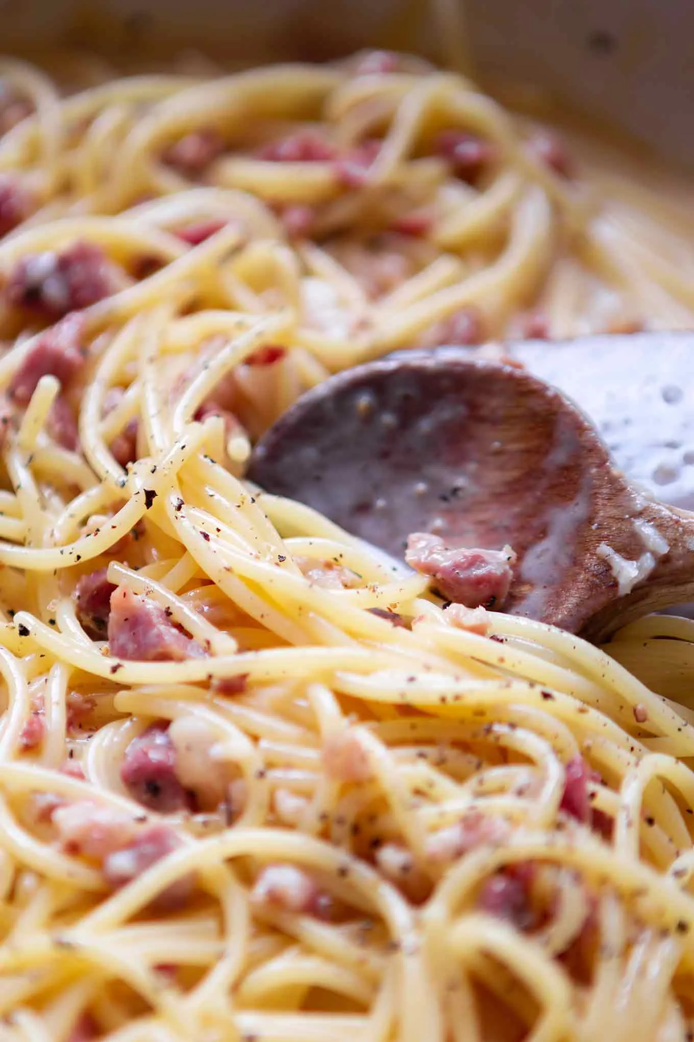 Frisch zubereitete Carbonara wird aus der Pfanne auf einen Teller gehoben, ein einfaches Pastarezept.