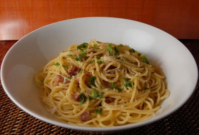 Frisch zubereitete Spaghetti Carbonara in einer rustikalen Schüssel, reichlich mit schwarzem Pfeffer bestreut und mit Parmesanspänen garniert.