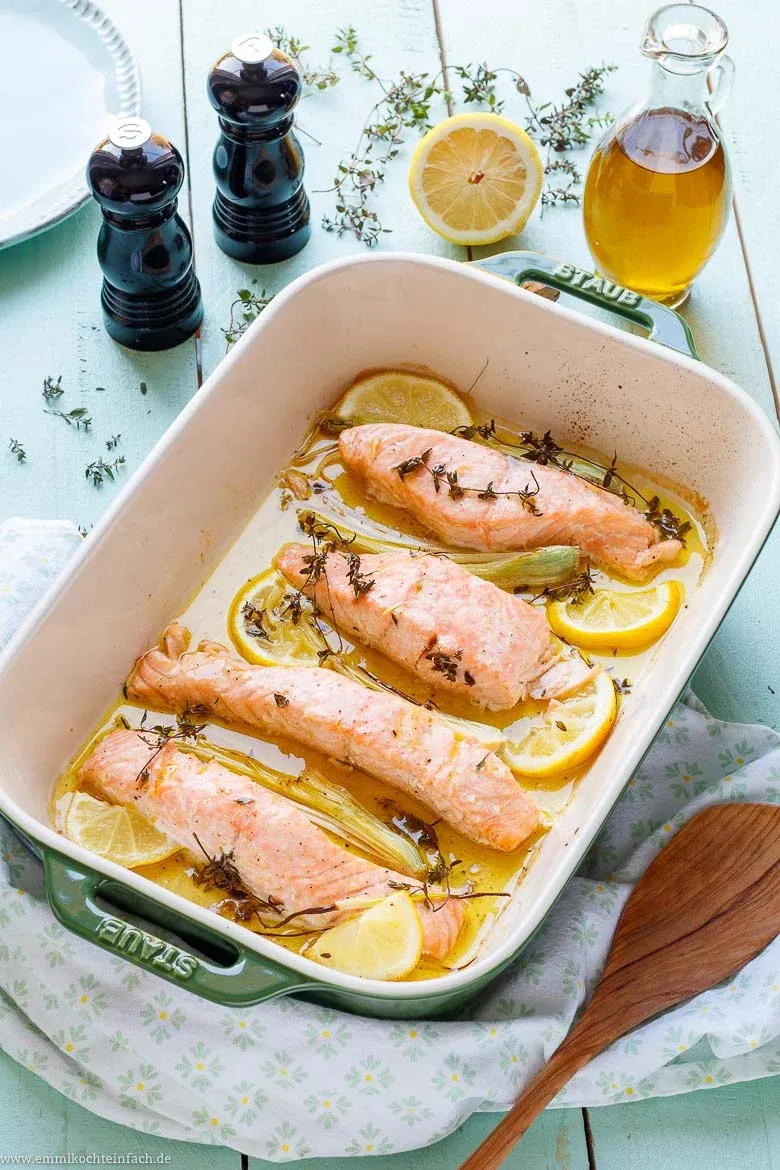 Frisch zubereitetes Lachsfilet aus dem Ofen mit Zitrone und Kräutern, serviert mit Baguette, ideal für ein gesundes Mittagessen oder Abendessen.