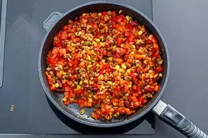 Frische Tomatenwürfel werden in die fertig gewürzte Hackfleisch-Gemüse-Mischung gerührt, um die Taco-Füllung zu vollenden.