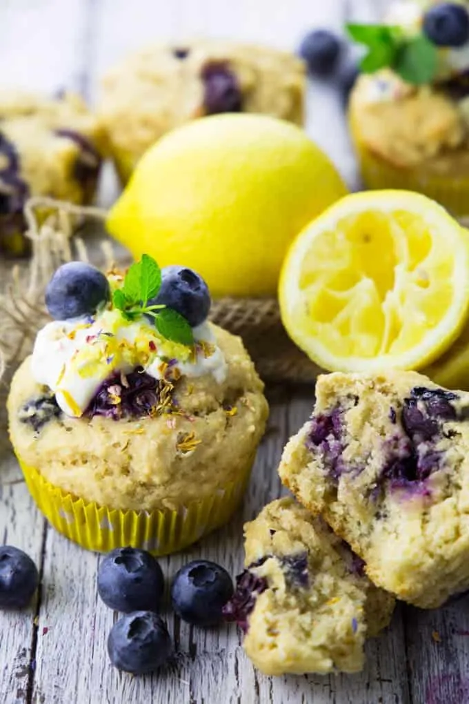 Frische vegane Blaubeer-Zitronen-Muffins auf weißem Holzbrett, umgeben von Zitronen und Blaubeeren