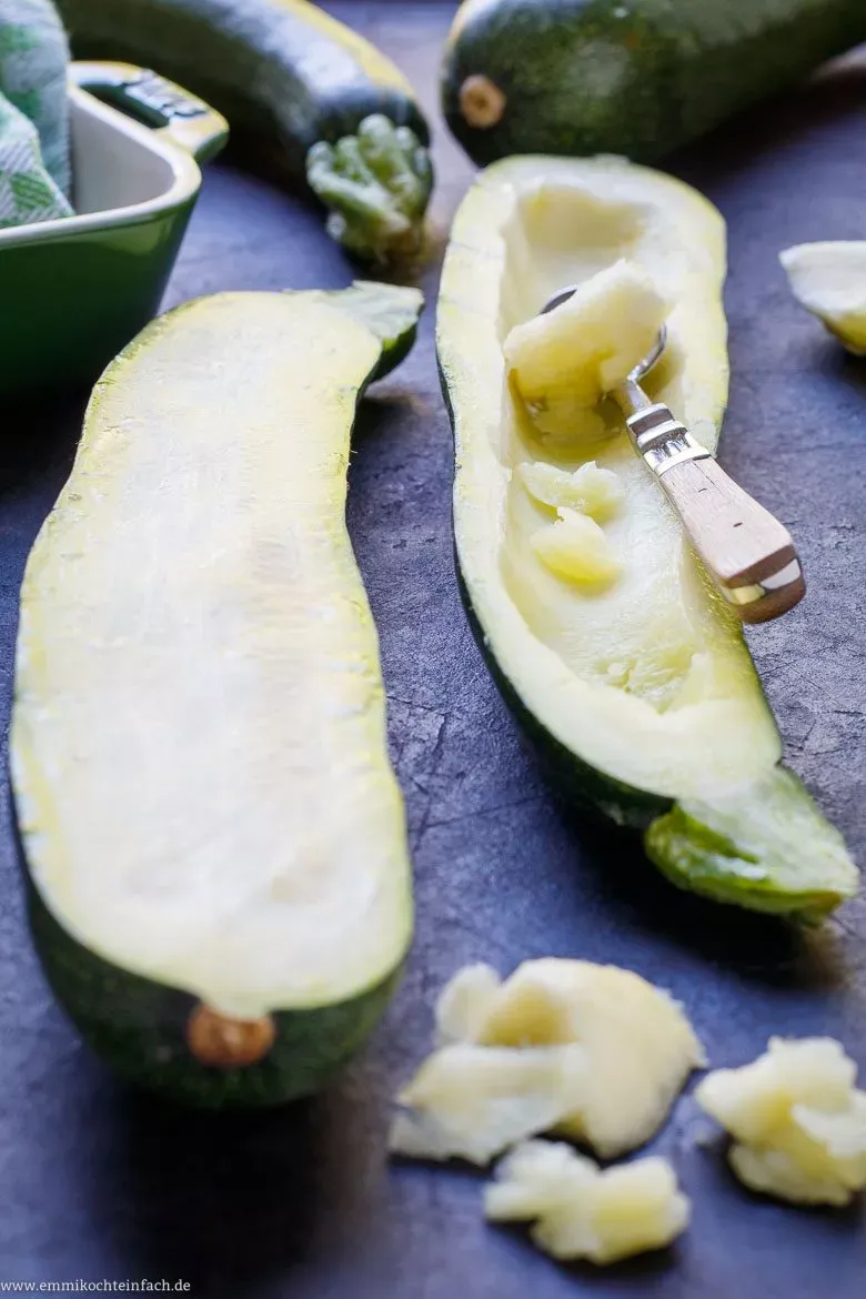Frische Zucchini-Hälften vor dem Füllen, teilweise ausgehöhlt mit dem Fruchtfleisch daneben