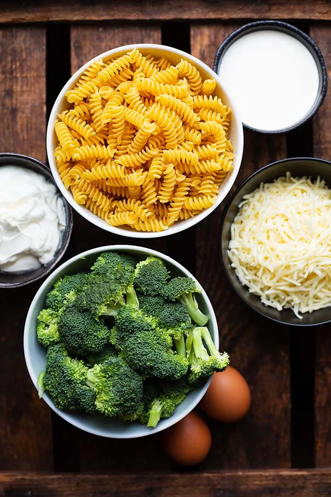 Frische Zutaten für den Brokkoli-Nudelauflauf: Fusilli, Brokkoli, Sahne, Schmand, Eier und geriebener Käse appetitlich angerichtet.