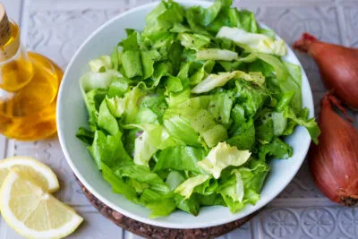 Frischer Endiviensalat auf einem Teller, umgeben von Schalotten, Zitrone, Honig und Senf für das Dressing.