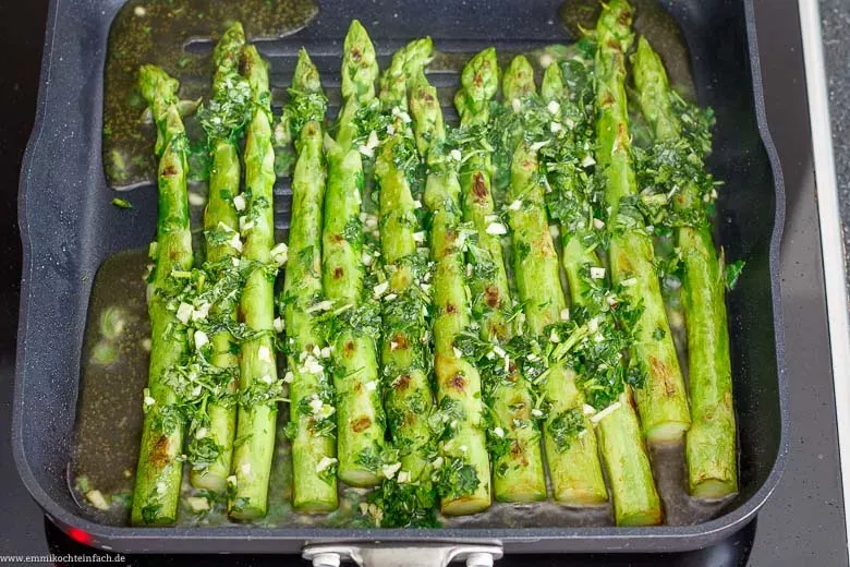 Frischer grüner Spargel brät in Olivenöl mit Petersilie und Knoblauch in einer Pfanne, bereit für einfache Spargelrezepte