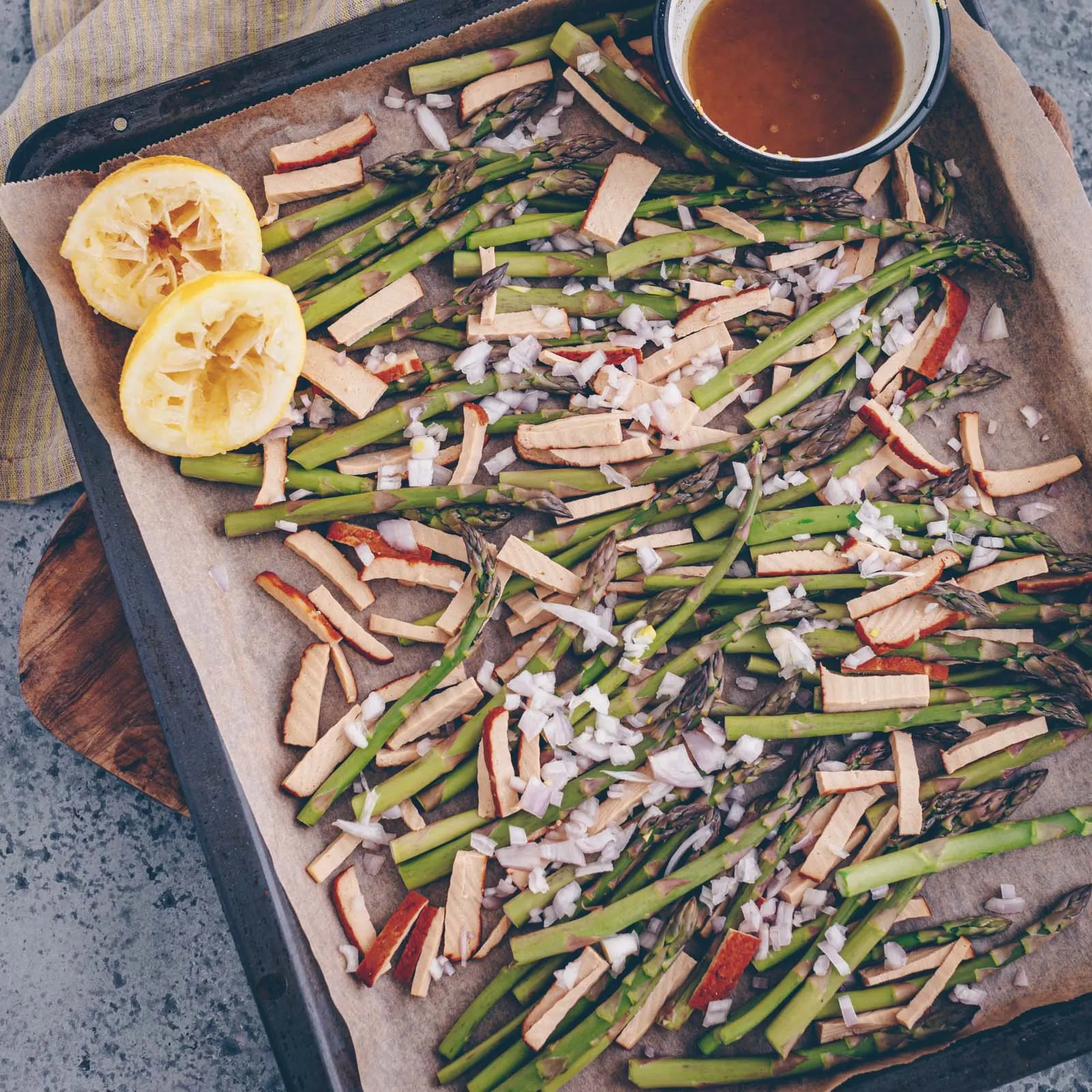 Frischer grüner Spargel, gewürfelter Tofu und Schalotten auf einem Backblech, bereit für den Ofen