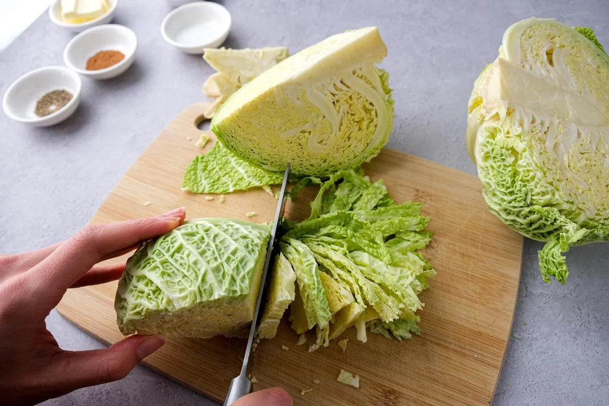 Frischer Wirsingkohl wird auf einem Holzbrett für Rahmwirsing geschnitten.