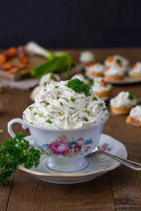 Frühlingskräuter-Aufstrich kunstvoll auf kleinen Brotscheiben arrangiert, garniert mit frischen Karottenscheiben und Kräutern