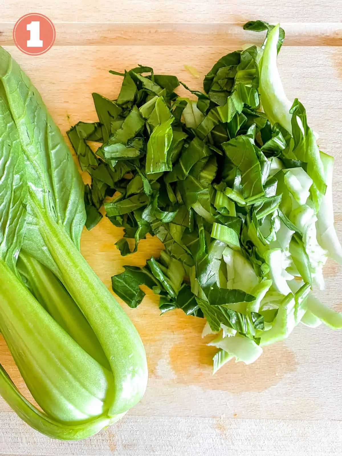 Ganze und fein gewürfelte Pak Choi Blätter und Stiele auf einem rustikalen Holzbrett, bereit zur Zubereitung des Salats.