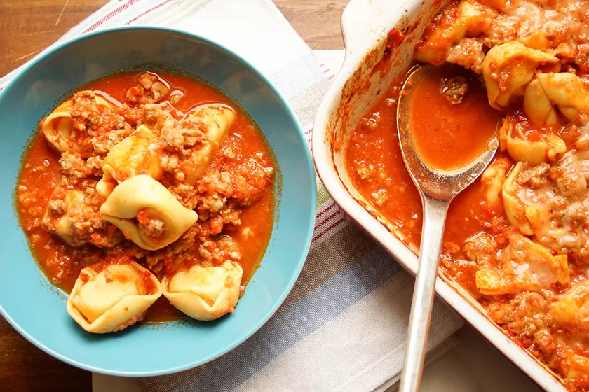 Gebackene Tortelloni mit Salsiccia-Tomatensoße in einer Auflaufform, bereit zum Servieren.
