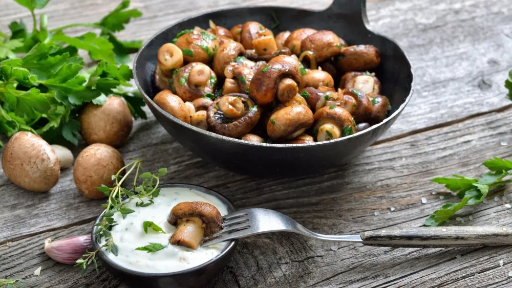 Gebratene Champignons mit Kräutern in einer dunklen Pfanne, bereit zum Servieren mit Sour Cream.