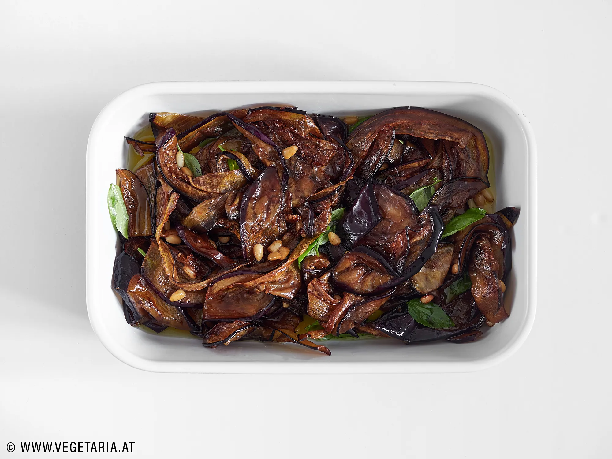 Gebratene Melanzani mit Basilikumblättern und Olivenöl in einer Schüssel.