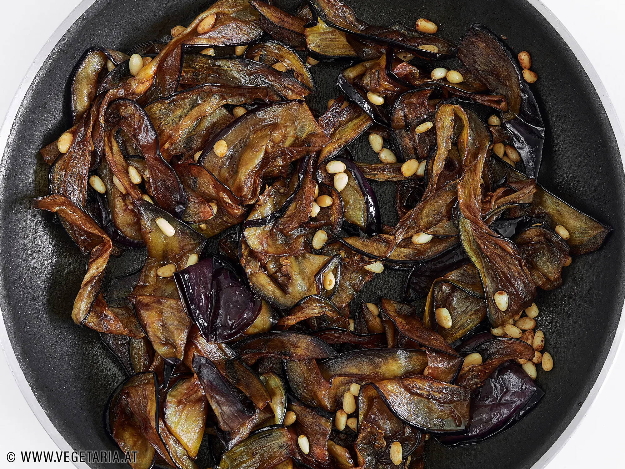 Gebratene Melanzanischeiben werden mit Balsamico-Essig in der Pfanne abgelöscht.