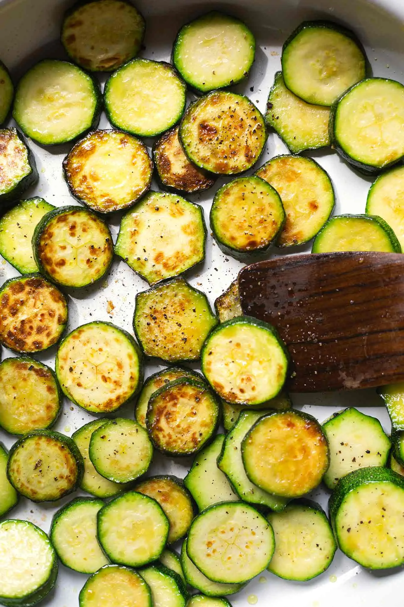 Gebratene Zucchini für die Zucchini-Hack-Pfanne in einer silbernen Pfanne. Die Zucchinischeiben werden mit einem Holz-Pfannenwender gewendet. Das Braten der Zucchini ist ein wichtiger Schritt für den Geschmack.