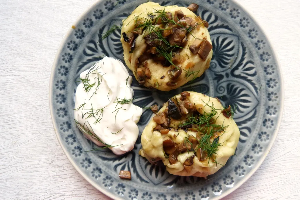 Gedämpfte Kolduny, gefüllte Teigschnecken, serviert mit einer cremigen Sauce und frischem Dill.