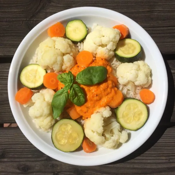 Gedämpfter Reis mit buntem Gemüse wie Brokkoli, Blumenkohl und Karotten, serviert mit einer roten Paprikasoße