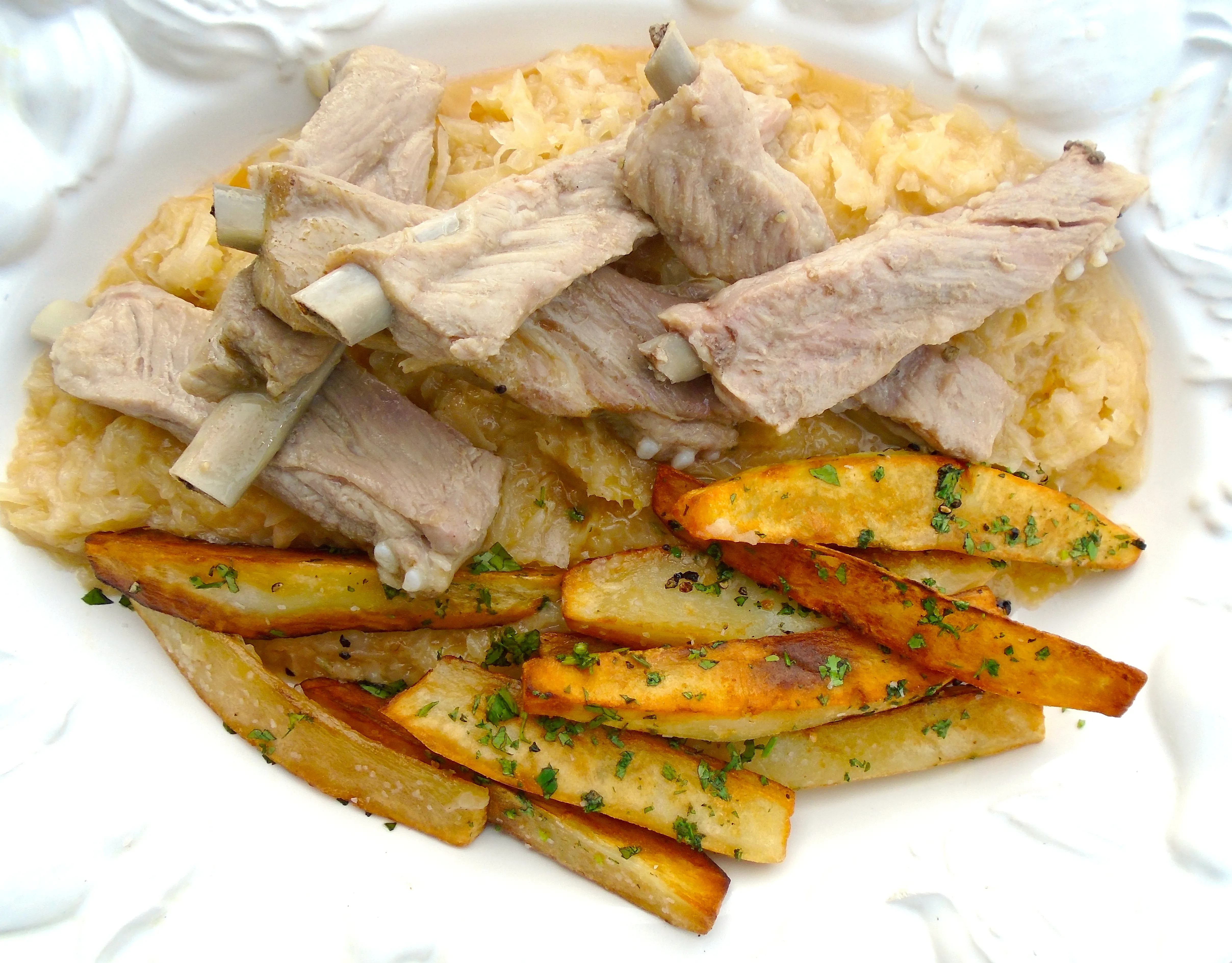 Gedünstete Schälrippchen auf Sauerkraut und Bratkartoffeln anrichten