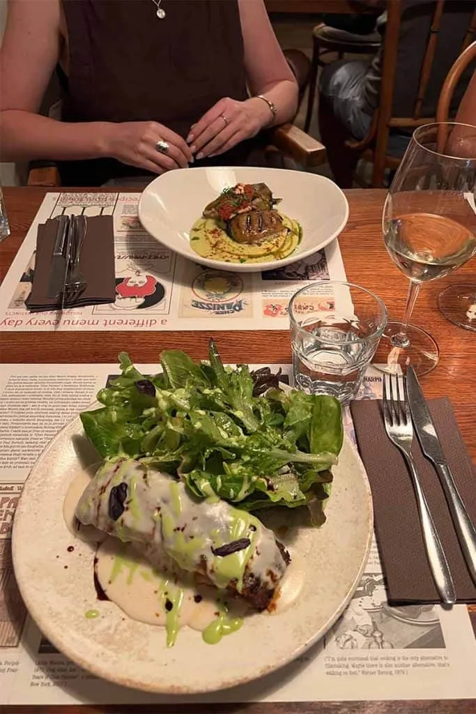 Gefüllte Paprika und Parmigiana, ansprechend auf zwei Tellern auf einem Holztisch im Mali Bar in Zagreb angerichtet, ein Beispiel für die vielfältige Küche.
