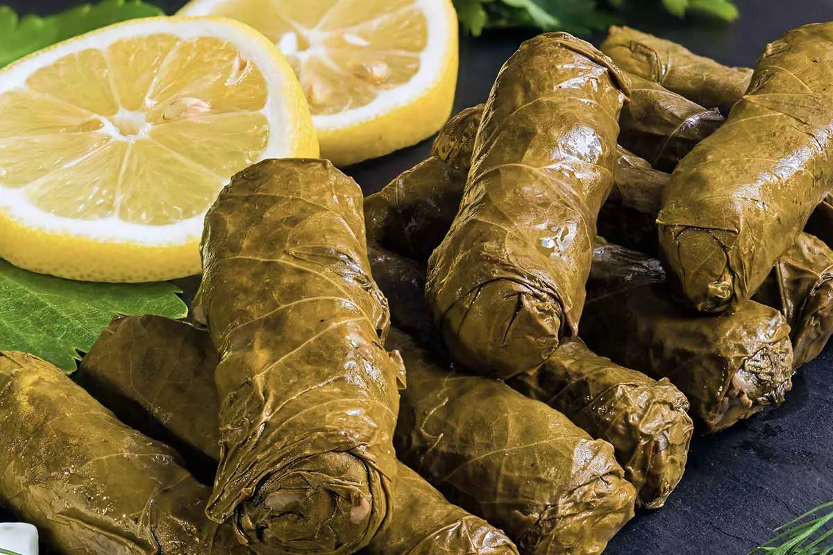 Gefüllte Weinblätter (Dolmades) mit Reis und Gewürzen, appetitlich angerichtet neben einer frischen Zitrone auf einem Teller, bereit zum Servieren.