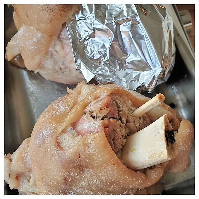 Gekochte Eisbeine, teilweise mit Alufolie bedeckt, vor dem Knusprigbraten.
