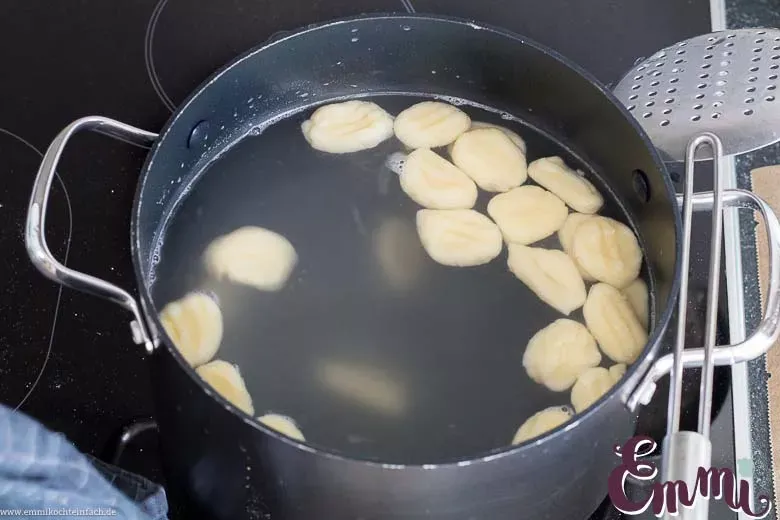 Gekochte Gnocchi schwimmen in einem Topf mit siedendem Wasser. Die dampfenden Gnocchi symbolisieren den Garprozess und die Vorfreude auf ein köstliches Gericht. Der Fokus liegt auf dem Moment des Kochens, um die Einfachheit und den Erfolg des Rezepts zu unterstreichen.