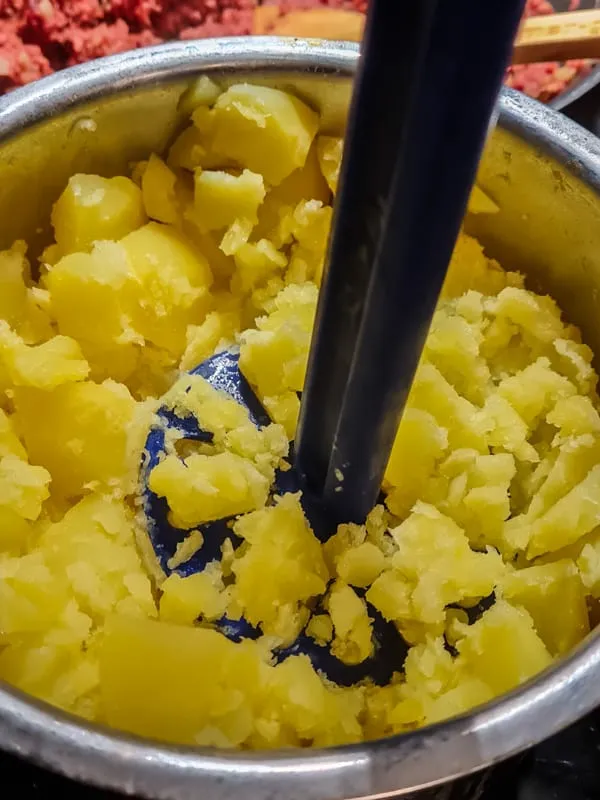 Gekochte Kartoffeln in einem Topf mit einem Kartoffelstampfer zerkleinern