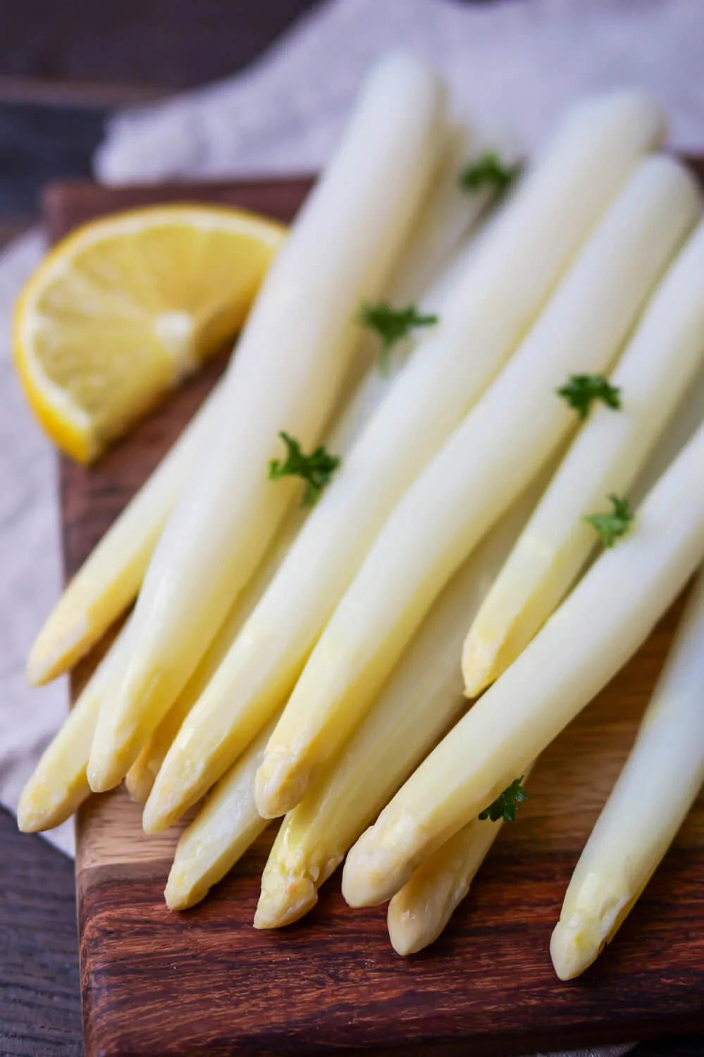 Gekochter weißer Spargel, angerichtet auf einem Holzbrett mit frischer Petersilie und Zitronenscheiben, bereit für den Garzeittest.