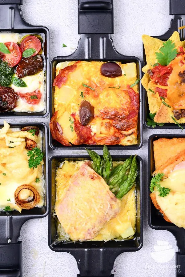 Gemütliches Raclette-Essen mit Freunden, appetitlich angerichteten Zutaten und Raclette Pfännchen bereit zum Überbacken.