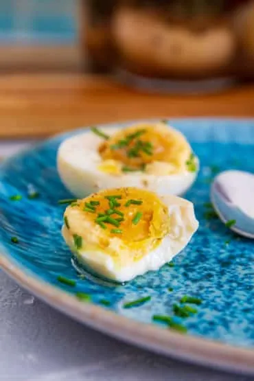 Genussfertige Soleier mit Schnittlauch, Brot und Butter auf einem Holztisch