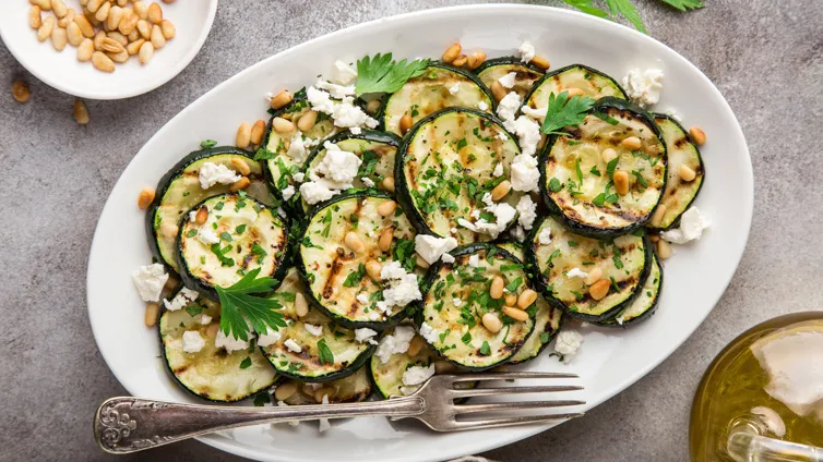 Gerillte Zucchini-Scheiben, bestreut mit Feta und frischen Kräutern, appetitlich angerichtet.