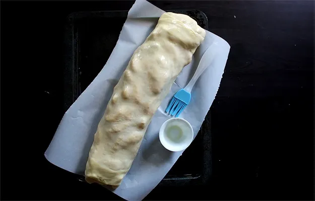 Gerollter Apfelstrudel wird vor dem Backen mit geschmolzener Butter bestrichen, für eine goldbraune Kruste im Strudel Rezept