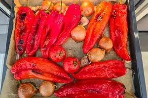 Geröstete Paprika, Tomaten und Knoblauch mit geschwärzter Haut auf einem Backblech nach dem Garen im Ofen