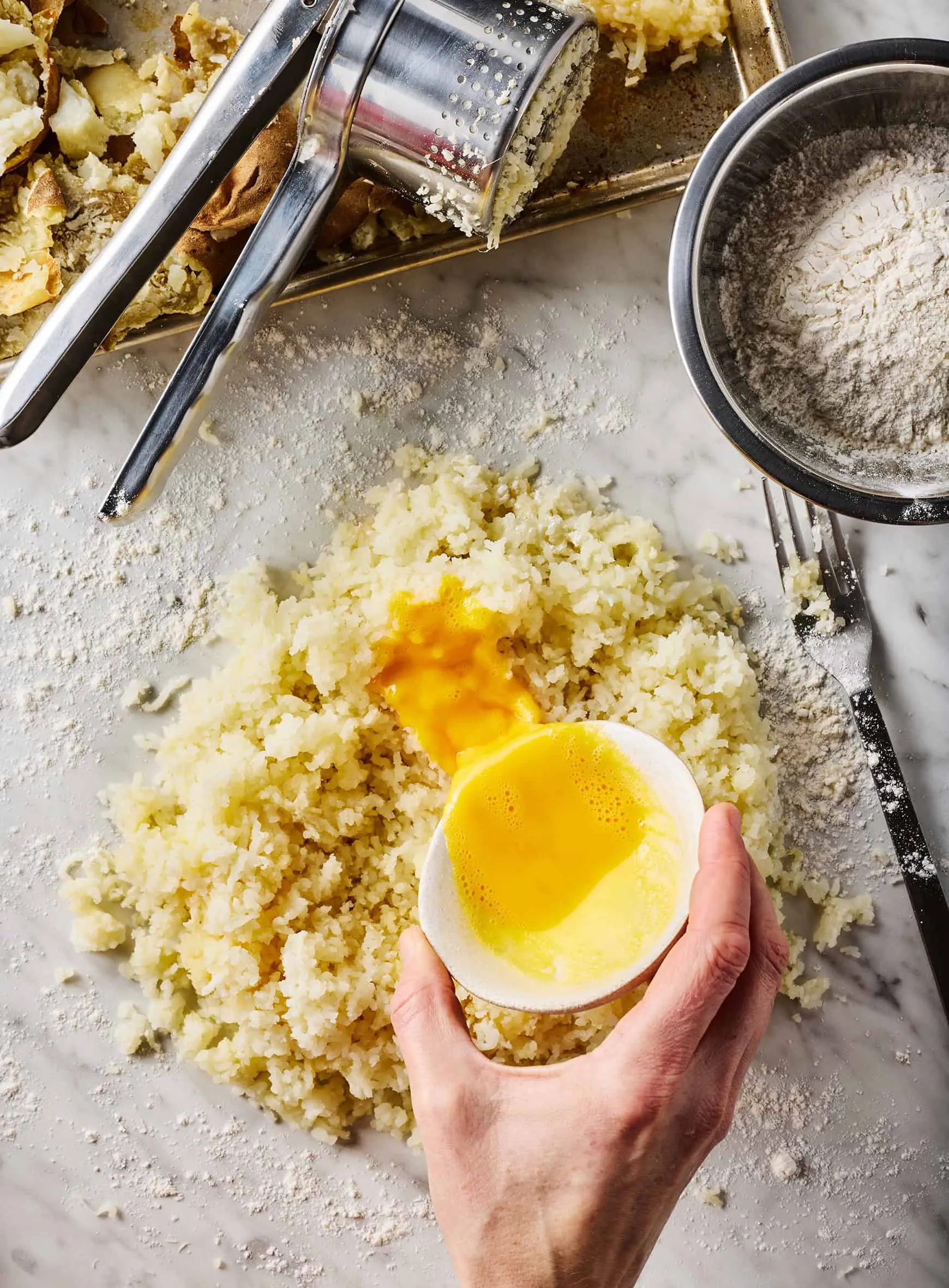 Geschlagene Eier werden über die geriebenen Kartoffeln auf einer bemehlten Fläche gegossen, bereit für den Gnocchi-Teig.