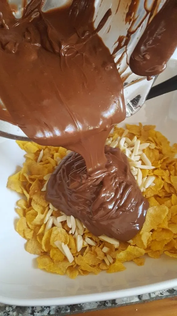 Geschmolzene Schokolade wird über die Cornflakes und Mandeln gegossen.