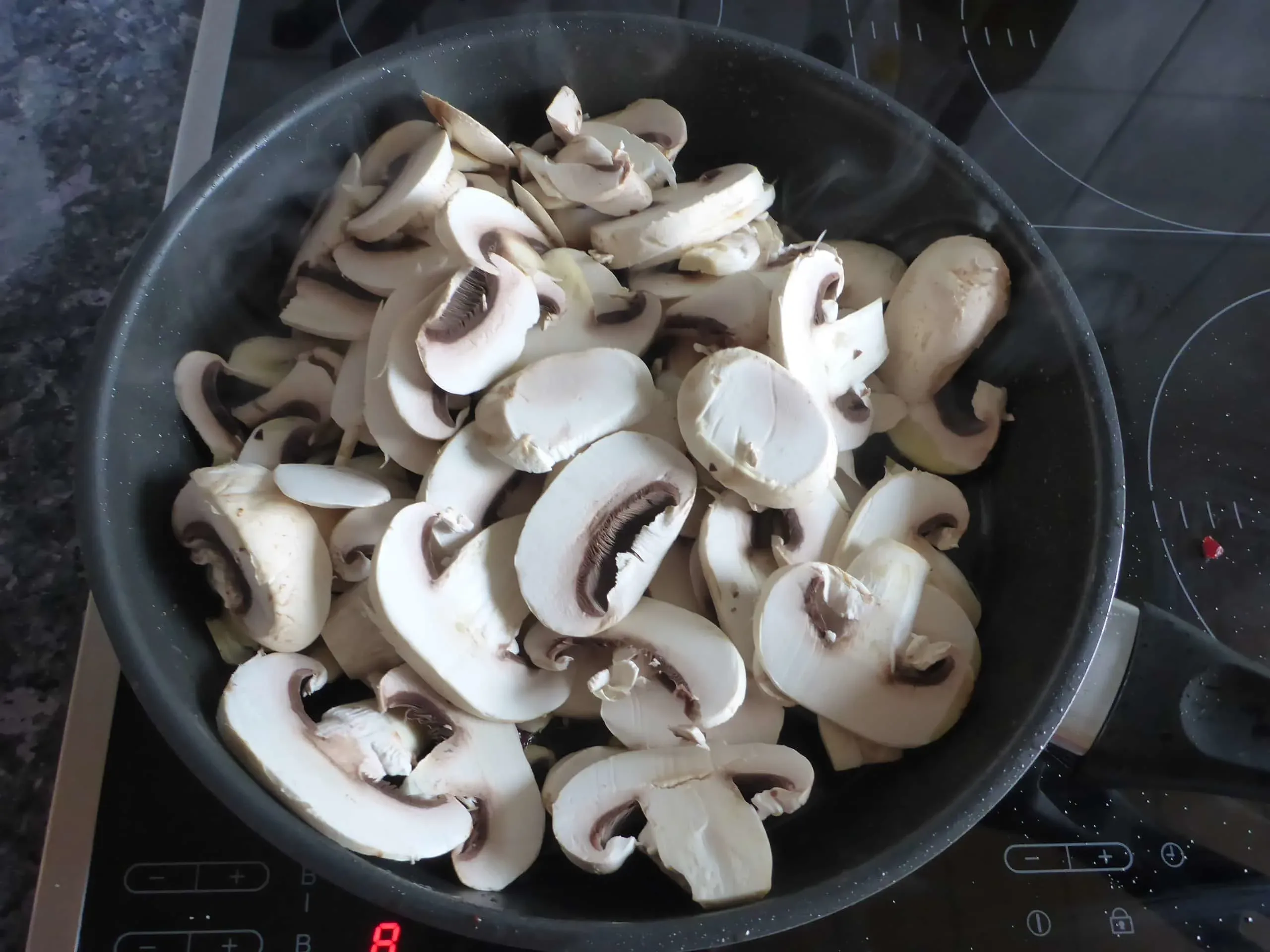Geschnittene Champignons werden im Speckfett angebraten, um eine geschmackvolle Basis für die Rahmsauce der Schnitzelpfanne zu schaffen.
