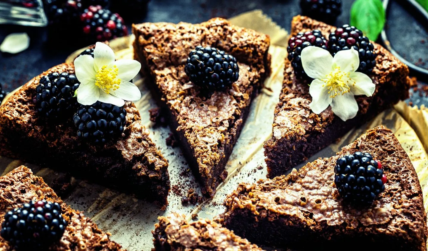 Geschnittener Schoko-Brownie-Kuchen, dekoriert mit Beeren und nicht essbaren Blumen.