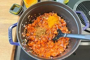 Gewaschene rote Linsen und duftende Gewürze wie Kurkuma und Kreuzkümmel werden im Topf mit dem angedünsteten Gemüse vermengt.