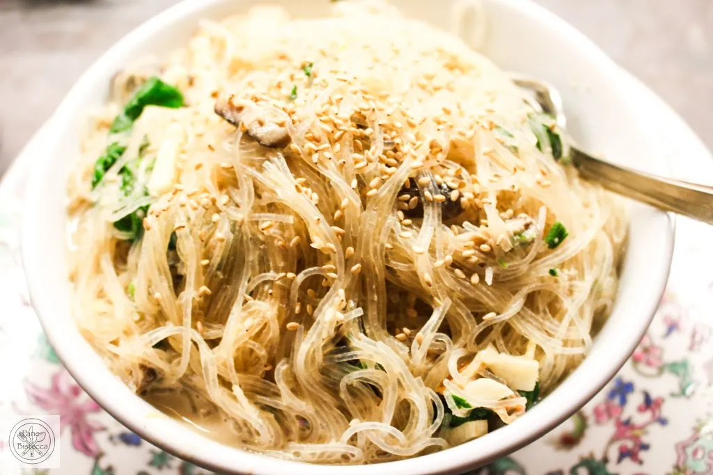 Glasnudeln werden sorgfältig mit der Spinat-Tahini-Sauce im Wok vermischt